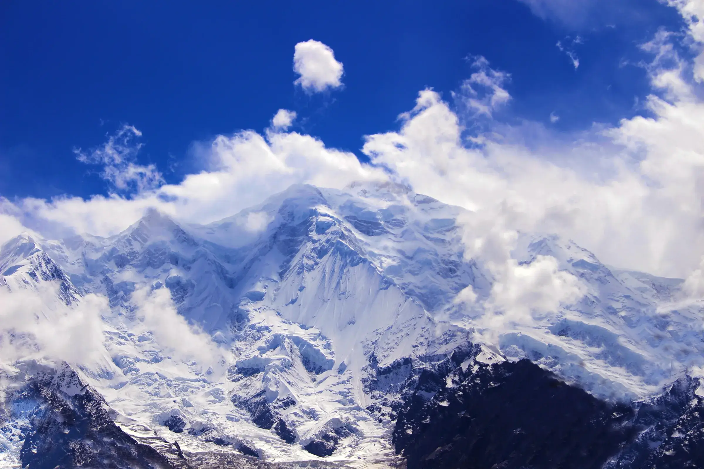 Snow-covered Rakaposhi rising beneath cloud and blue sky.