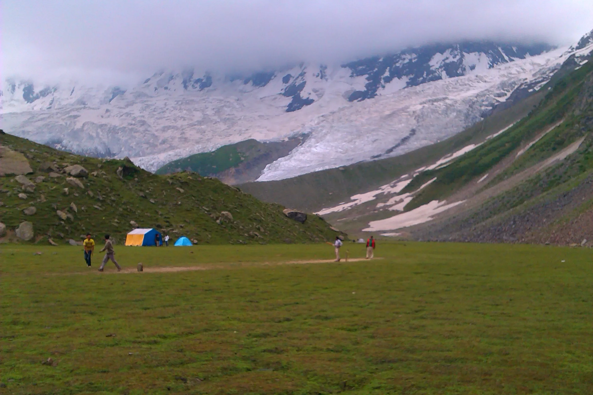 Tents on grassland below a glacier on the Rakaposhi base-camp trek.